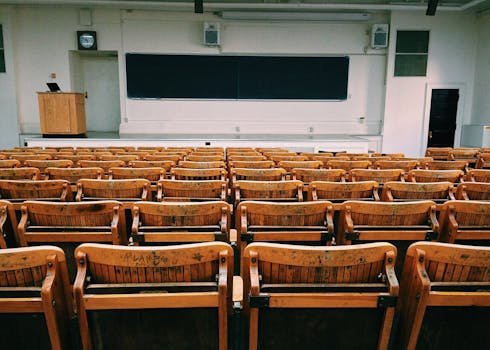 An empty lecture hall featuring wooden chairs and a large blackboard.