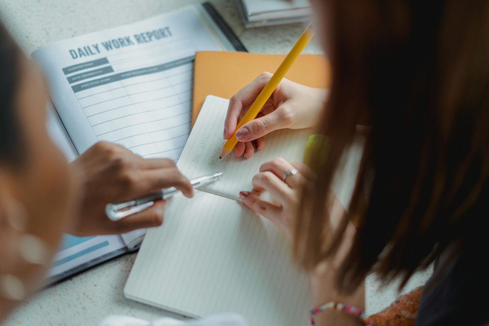 Two individuals collaborate during a study session, using notebooks and daily work reports.
